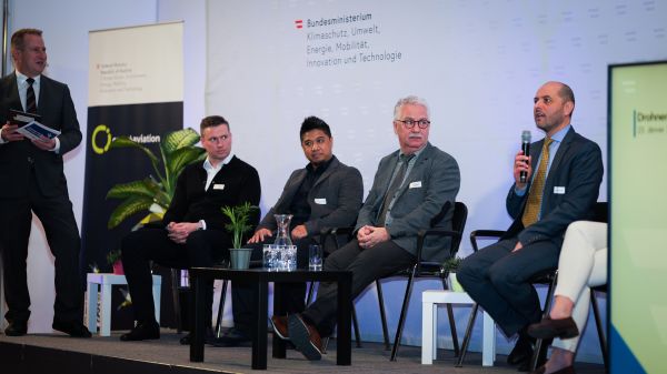 Podiumsdiskussion: Ein Mann steht, während vier weitere auf der Bühne sitzen, einer hällt das Mikrofon.