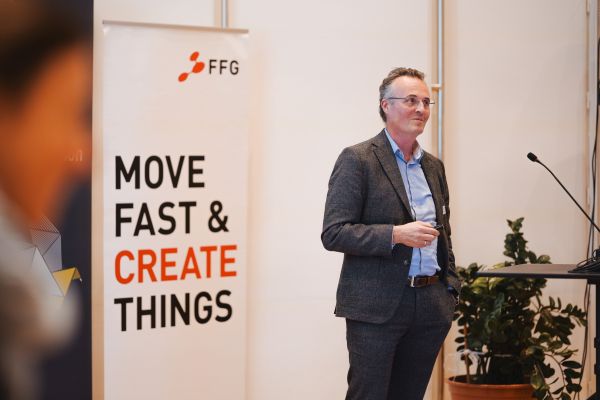 Ein Mann Mit Sakko und blauem Hemd steht beim Rednerpult.