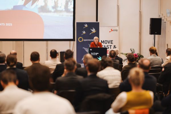 Frau mit kurzen weißen Haaren, rotem Pulli und schwarzer Hose spricht am Rednerpult.