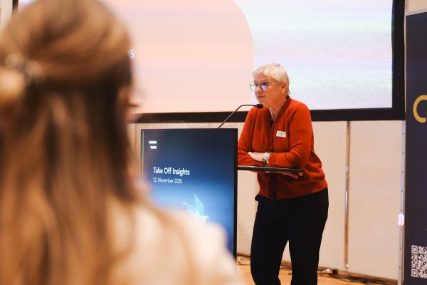 Frau mit kurzen weißen Haaren, rotem Pulli und schwarzer Hose spricht am Rednerpult.