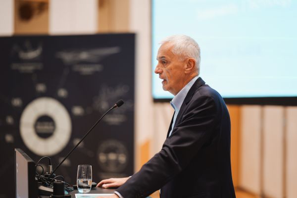 Mann mit weißen Haaren spricht ins Microphon beim Rednerpult.