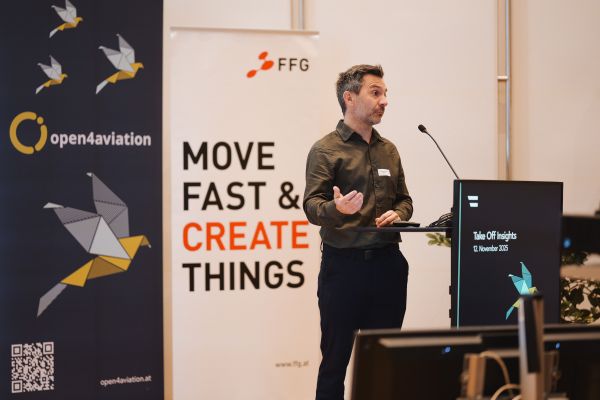 Ein Mann mit kurzen dunklen Haaren, grünem Shirt und schwarzen Hosen spricht ins Microphon.