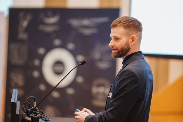 Ein Mann mit Bart Sakko und schwarzem Hemd spricht am Rednerpult.