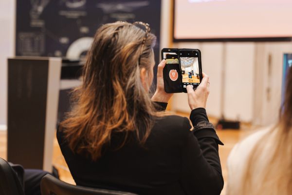 Eine Frau im Publikum fotografiert die Rednerin mit ihrem Handy.