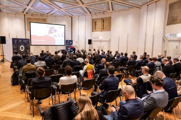 Der ganze Veranstaltngsraum von Hinten mit Blick auf die Bühne. Das Publikum sitzt in Stühlen.