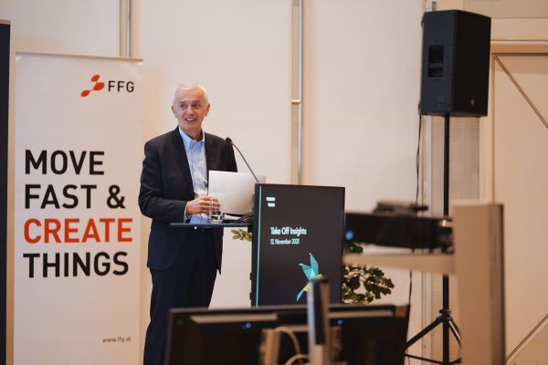 Mann mit weißen Haaren spricht ins Microphon beim Rednerpult.