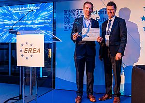 Zwei Männer schauen in die Kamera, einer hält den EREA Best Paper Award Award in den Händen.